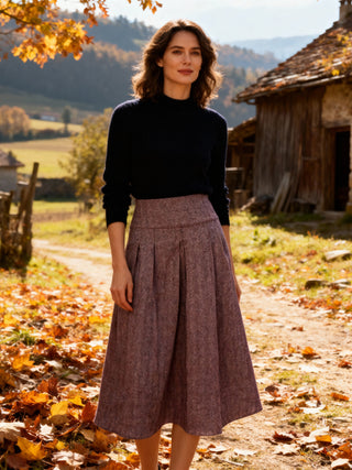 Woman standing in a scenic outdoor setting with autumn leaves and a wooden cabin.