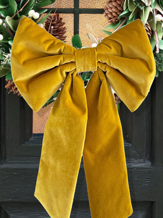 Large yellow velvet bow with greenery and pinecones on a dark surface