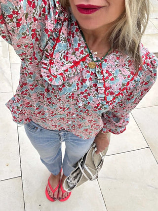 Woman wearing a floral blouse and jeans on a tiled floor.
