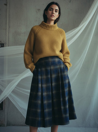 Woman wearing a mustard yellow sweater and blue plaid skirt against a plain background