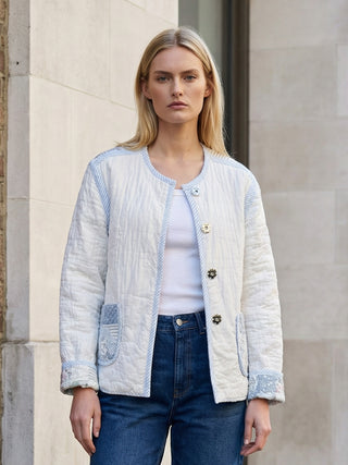 Woman wearing a light blue quilted jacket and dark jeans standing against a stone wall.