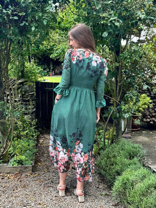 Woman wearing a green floral dress standing in a garden.