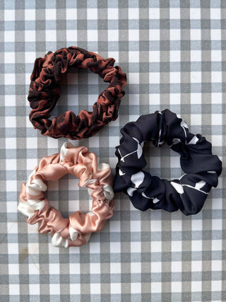 Three scrunchies in brown, pink, and black on a checkered background