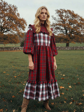 Woman wearing a red plaid dress standing in a field with trees in the background