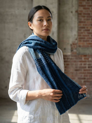 Woman wearing a blue scarf in an indoor setting with brick walls.