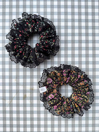 Two black lace scrunchies with floral patterns on a checkered background