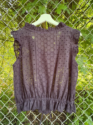 navy sleeveless top with black polka dots on a hanger against a green leafy background.