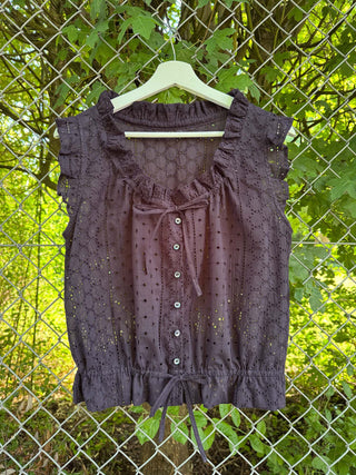 navy sleeveless top with buttons on a hanger against a chain-link fence and greenery background