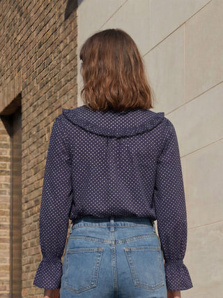 Person wearing a polka dot shirt and jeans standing against a brick wall.