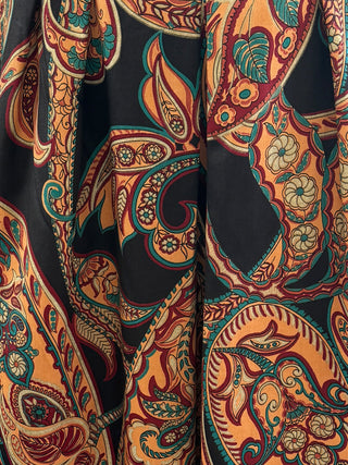 Close-up of a patterned fabric with intricate designs in orange, red, and green on a black background.