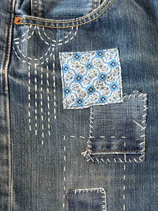Close-up of a blue denim pocket with floral patch and decorative stitching