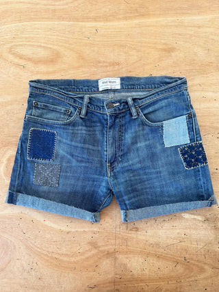 Pair of blue denim shorts with patchwork design on a wooden surface