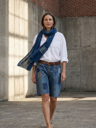 Woman wearing a white shirt, blue denim shorts, and a blue scarf in an urban setting.