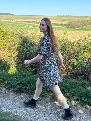 Model walking in UK-made floral mini dress with subtle ruffle detail.