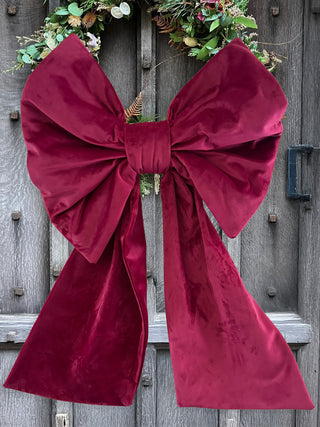 Large burgundy velvet bow on a wooden door with wreaths.