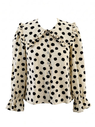 A women's long-sleeve blouse with a black polka dot pattern on a cream base, featuring a large ruffled collar and ruffled cuffs, shown against a plain white background.