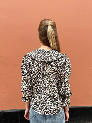 Person wearing a leopard print blouse against a brown wall