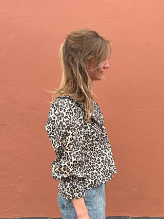 Person wearing a leopard print blouse against a brown wall