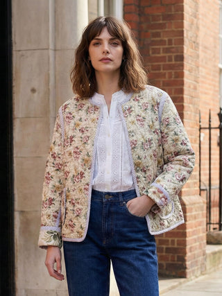 Woman wearing a floral jacket and blue jeans standing against a brick wall.