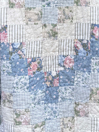 Patchwork quilt with floral and gingham patterns in blue, pink, and white.