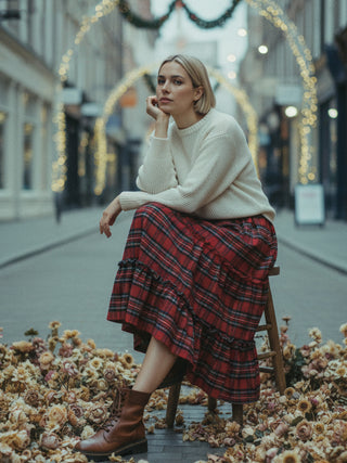Woman sitting on a stool in an urban setting with festive lights and autumn leaves.