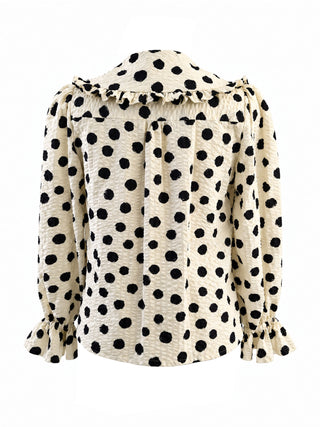 A long-sleeve blouse with a black polka dot pattern on a cream background, featuring a ruffled collar and ruffled cuffs, shown against a plain white background.