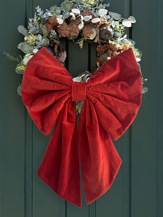 Decorative wreath with a large red bow on a green door