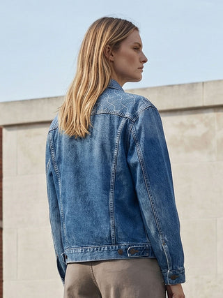 Person wearing a blue denim jacket standing against a light-colored wall.