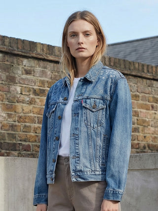 Woman wearing a blue denim jacket against a brick wall.