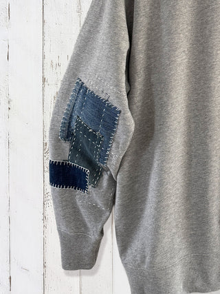 Gray sweatshirt with denim patch on sleeve against a wooden background