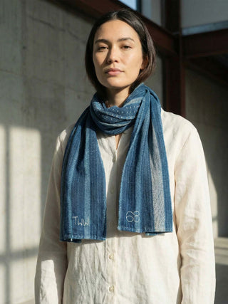 Woman wearing a blue scarf with visible branding, standing indoors.