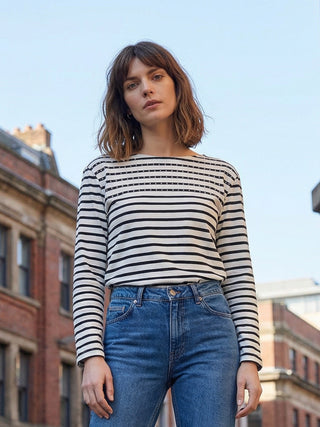 Woman wearing a striped shirt and jeans standing outdoors with buildings in the background