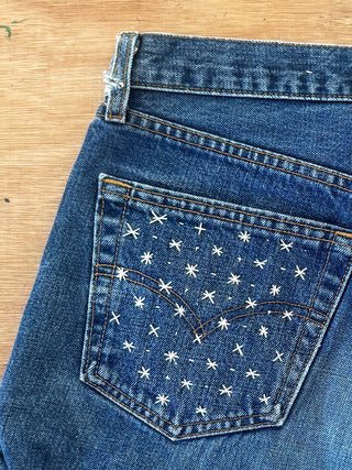 Close-up of blue jeans with white star pattern on pocket on a wooden surface
