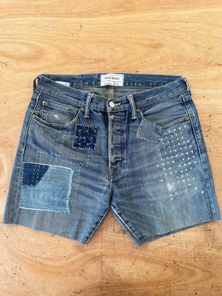 Pair of blue denim shorts with patchwork design on a wooden surface