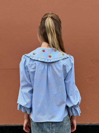Person wearing a blue striped shirt with crochet strawberries against a brown background