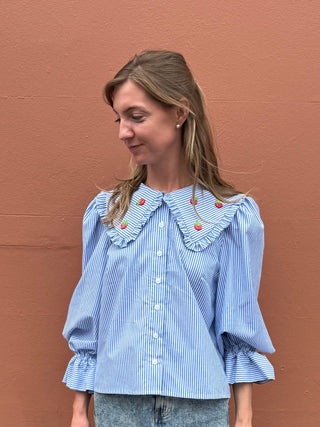 Woman wearing a blue striped blouse with a decorative collar against a brown background