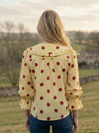 Person wearing a yellow blouse with red patterns in an outdoor setting