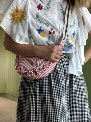 Person wearing a white embroidered shirt and black and white checkered skirt, holding a pink and white striped bag.
