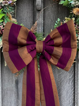 Large purple and bronze striped bow on a wooden door with floral decorations.