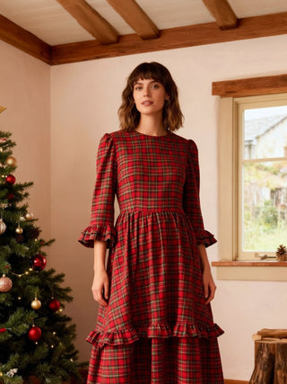 Woman wearing a red plaid dress in a room with a Christmas tree and window.