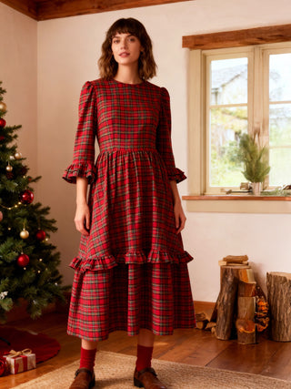 Woman wearing a red plaid dress in a room with a Christmas tree and window.