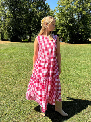 Woman wearing a red checkered dress standing on grass with trees in the background