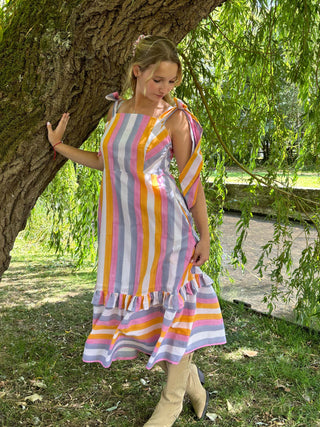 The Mila Dress styled outdoors – slow fashion summer outfit in cheerful rainbow cotton, worn barefoot in a garden setting.