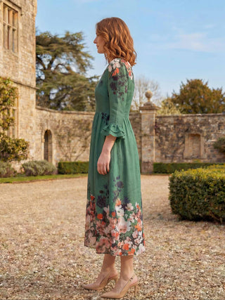 Woman in a green floral dress standing in front of a historic building.