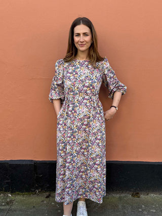 Model wearing The Maisie Dress – a floral midi dress made from deadstock cotton, styled with white trainers.
