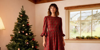 Woman in a red plaid dress standing next to a decorated Christmas tree indoors.