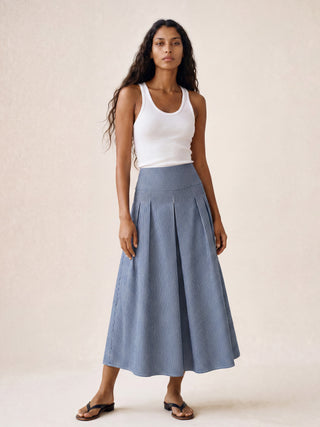 Woman wearing a white tank top and blue skirt on a beige background