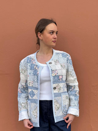 Model wearing a reversible quilted jacket made from a reworked vintage quilt in soft blue floral patchwork, handmade in the UK by The Well Worn.