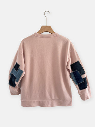 Pink sweatshirt with black and blue patchwork sleeves on a hanger against a white background