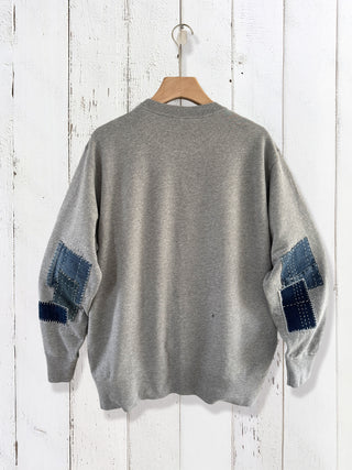 Gray sweater with blue patch details on a wooden hanger against a white wooden background
